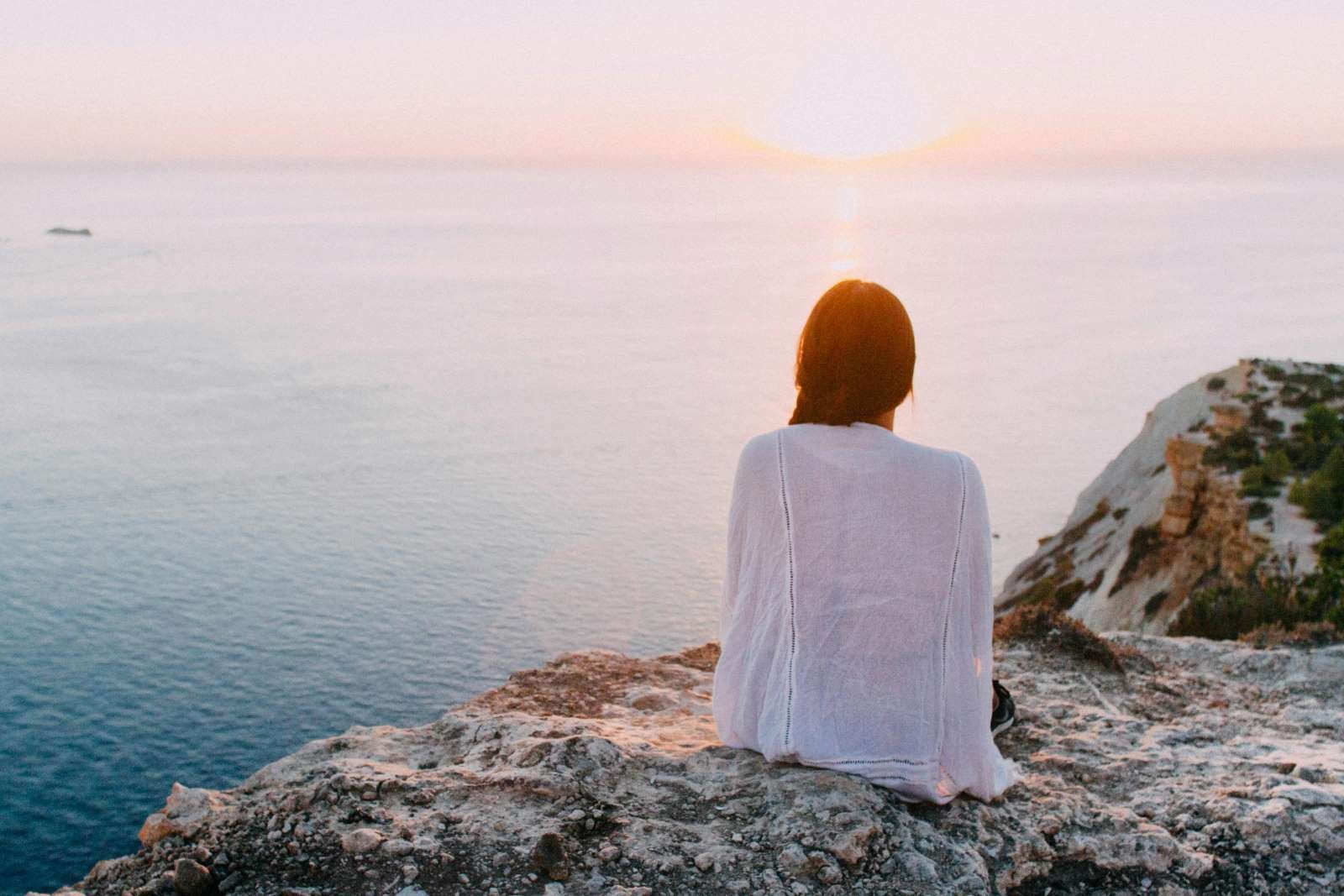 Woman Sitting on Gray Rock Near Body of Water